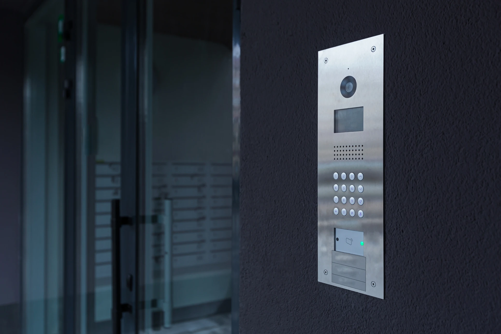 Entrée d'immeuble moderne avec interphone vidéo numérique installé sur mur texturé sombre