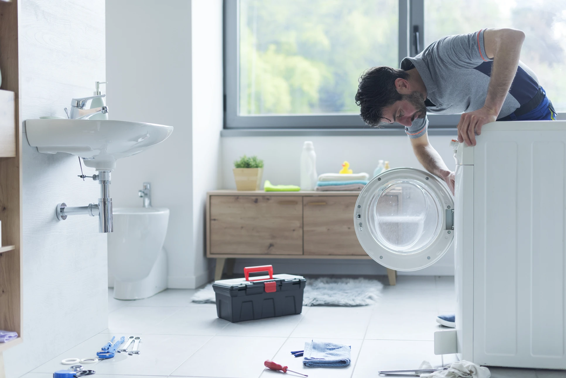 Technicien en combinaison bleue et gants de protection répare une machine à laver blanche dans une buanderie domestique