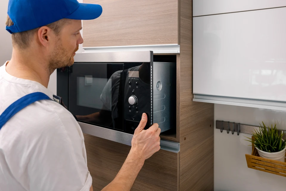 Technicien en salopette bleue installant un four encastrable dans une cuisine moderne blanche